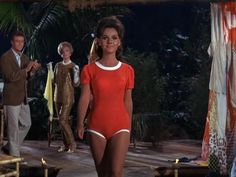 a woman in a red bodysuit walking down a runway with other people behind her