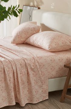 a bed with pink sheets and pillows in a room next to a potted plant