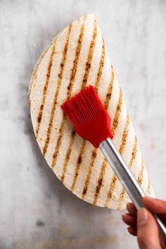 a hand holding a red brush on top of a tortilla