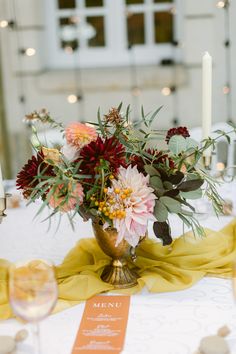 a vase filled with lots of flowers on top of a white table cloth next to candles