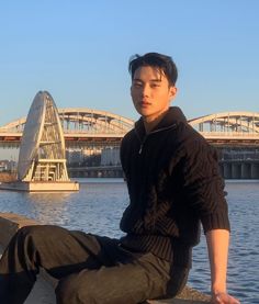 a young man sitting on the edge of a pier next to a body of water