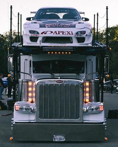 a large truck is parked in a parking lot with other cars behind it and people standing around