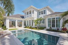 a large white house with a swimming pool in the front yard and palm trees surrounding it