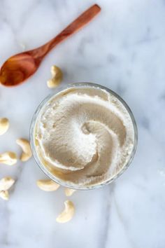 a glass cup filled with whipped cream and nuts next to a spoon on a marble surface