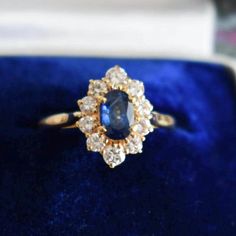 a ring with an oval shaped blue stone surrounded by small white and yellow diamonds in a velvet box