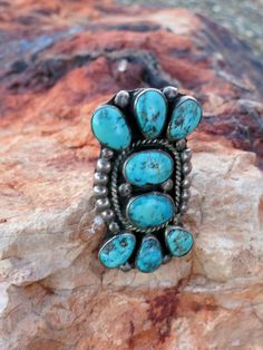 This is an exquisite VINTAGE NAVAJO BEAUTY, Turquoise Ring with 8 cabochons beautifully set in a regal design with twisted silver rope frame and Navajo "raindrop" ( silver beads) accents. Circa 1940-50's Sz 7, Sterling1 7/8" L x 1" W 13.2 GramsPre-owned in excellent condition, Some Patina No damage.Ships USPS Priority Insured mail Vintage Oval Turquoise Gemstone Ring, Vintage Oval Turquoise Ring Collectible, Retro Turquoise Jewelry For Collectible, Retro Turquoise Jewelry Collectible, Retro Turquoise Jewelry For Collectors, Vintage Oval Turquoise Cabochon Ring, Vintage Oval Cabochon Turquoise Ring, Vintage Hallmarked Turquoise Ring, Vintage Hallmarked Turquoise Ring For Collectors