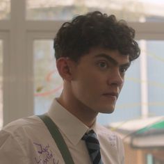 a young man with curly hair wearing a shirt and suspenders looking at the camera