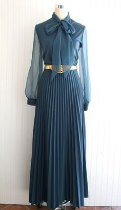 "Circa 1970s, this is a teal dress with perma peleat skirt and sheer sleeves and bow at the neckline.   We have paired it with a gold blet that is not original and is not included.  This dress is without holes or stains.  It is missing it's original belt or sash.  Marked size 14 Estimated size 12 38\" bust 30\" waist full hip 57\" nape to hem  Purveyor's Note: We have searched far and wide, wrestled bears, braved the cold, traversed mountain ranges, fought pirates, swam with sharks and eaten at many a questionable road side taco stand to provide our customers with one of a kind vintage pieces.  Know that whichever piece you choose to make your own has its own story and has traveled through time to get to you.  Though we strive to provide the absolute best, \"pristine\" vintage pieces are r Vintage Teal Dress, Vintage Pleated Party Dresses, Retro Evening Dress For Fall, Vintage Pleated Dress For Party, Pleated Vintage Dress For Party, Chic Vintage Evening Dress For Fall, Chic Fall Dresses For Vintage Fashion, Retro Dresses For Vintage Events In Fall, Retro Fall Dresses For Vintage Events