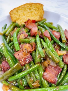 a white plate topped with green beans covered in bacon next to a piece of bread