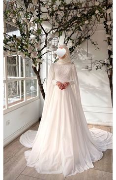 a woman in a white wedding dress standing next to a tree with flowers on it