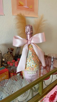 a bottle with a pink bow on it sitting on a shelf next to glasses and other items