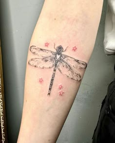 a small dragonfly tattoo on the right arm and leg, with pink stars around it