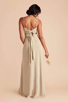 the back of a woman wearing a beige dress with a bow at the waist and spaghetti straps