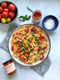 a plate of pasta with tomatoes, parmesan cheese and seasoning on the side