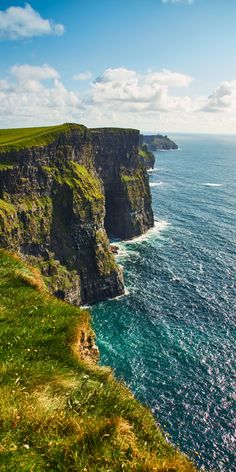 an ocean cliff with green grass on the side and blue water in the foreground