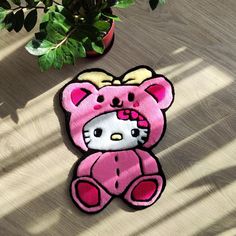 a pink hello kitty rug sitting on top of a wooden floor next to a potted plant