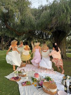 a group of women in dresses are dancing around a table with food and drinks on it