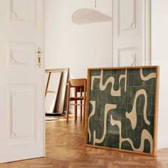 a room with white walls and wooden floors has a framed painting on the floor next to two chairs