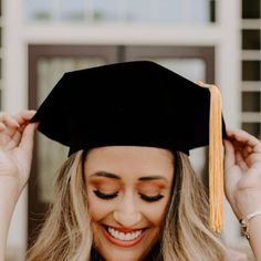 a woman wearing a graduation cap and gown with her hands on her head, smiling at the camera