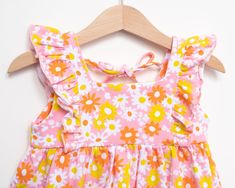 Sport a groovy outfit this summer with this flower power pink girls dress. The perfect colorful vintage style dress to add some fun and cheeriness to her wardrobe. Made from a soft and stretchy cotton spandex fabric blend, she will be comfy enough to play all day, but look stylish doing so. 95% Cotton 5% Spandex Tie back closure - not intended for sleeping Imported INSPIRED BY YESTERDAY, DESIGNED FOR YOUR BABY TODAY You will love dressing your little girl in the fun styles at Strawberry Jam Kids Pink Girls Dress, Toddler Girl Romper, Summer Baby Clothes, Yellow Tie, Girls Pink Dress, Flutter Dress, Cute Pants, Yellow Ties, Girls Dresses Summer