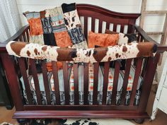 a baby crib with a cow print blanket on it's back and pillows hanging from the rails