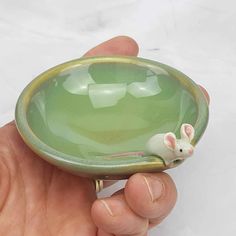 a hand holding a small green bowl with a mouse in it