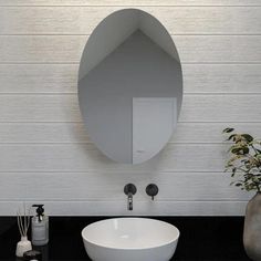 a white sink sitting under a round mirror next to a vase with flowers in it