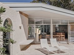 two white lounge chairs sitting in front of a house