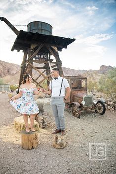 a man and woman standing next to each other near an old truck in the desert