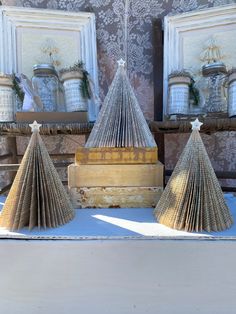 three christmas trees made out of books sit on a table in front of two framed pictures