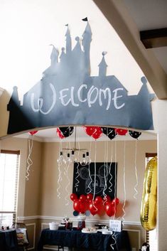 a welcome sign with balloons and streamers hanging from it's ceiling in a room