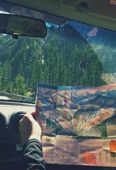 a person is holding up a map while driving in a car with mountains and trees behind them