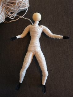 a white doll laying on top of a bed next to a ball of string and yarn