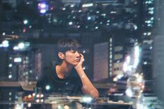 a young man sitting at a table with his hand on his chin looking out the window