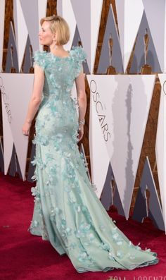 a woman in a blue dress on the red carpet at an oscars event, looking off to the side