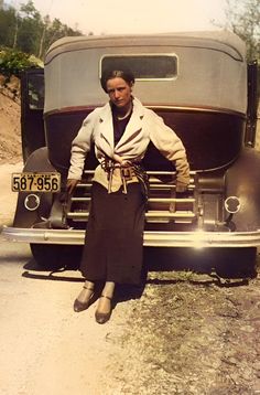 an old photo of a woman leaning on the hood of a car in front of her