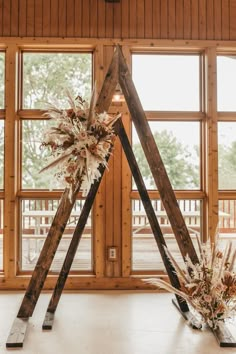 two tall wooden poles with dried flowers in them on top of a white floor next to large windows