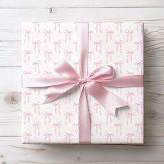 a wrapped gift box with pink ribbon and bow on white wooden background, top view