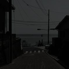 an empty street with power lines above it and the ocean in the background at night