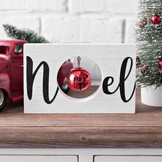 a wooden sign that says noel with a red ornament hanging from it's center