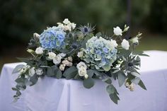 a bouquet of blue and white flowers sitting on top of a table covered in greenery