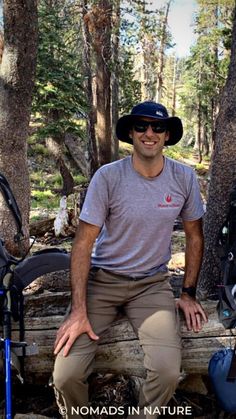 a man sitting on a log in the woods with his bike and backpack behind him