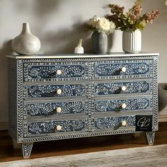 an ornate blue and white dresser with flowers in vases