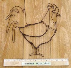 a metal rooster sculpture sitting on top of a wooden floor next to a measuring ruler