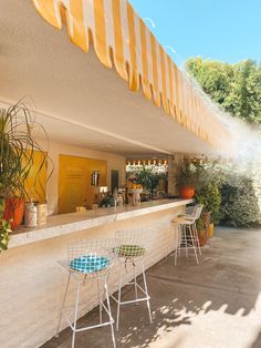 an outdoor bar with chairs and umbrellas on the outside wall, next to potted plants