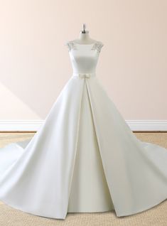 a white wedding dress on display in front of a pink wall and beige carpeted floor