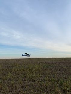 an airplane is flying low in the sky above a field with grass and weeds on it