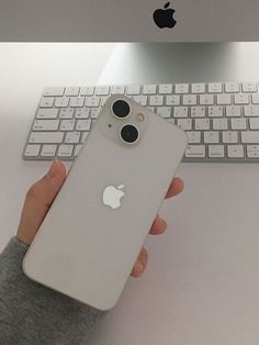 a person holding an iphone in front of a keyboard and computer monitor with the apple logo on it