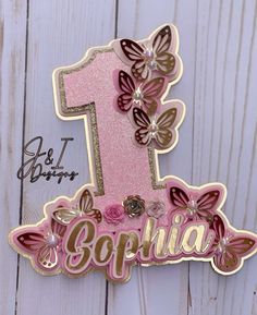 a pink and gold birthday card with the number one on it's side, decorated with butterflies