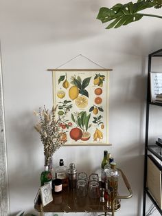 a bar cart with bottles and glasses on it in front of a wall mounted poster